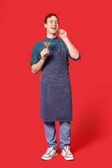 Young male bartender holding glass of martini with olives on red background