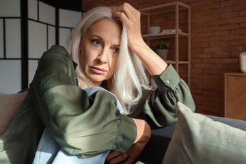 Depressed mature woman sitting on sofa at home, closeup - obrazy, fototapety, plakaty