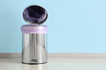 Modern trash bin with foot pedal and open lid near blue wall