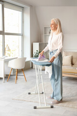 Happy mature woman ironing clothes at home