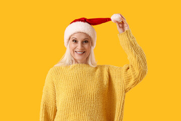 Mature woman in Santa hat on yellow background