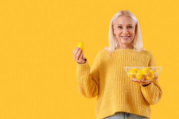 Mature woman holding basket with lemons on yellow background