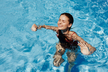 Happy woman swimming in pool in red swimsuit with loose long hair, skin protection with sunscreen, concept of relaxing on vacation.