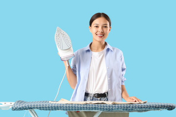 Young Asian woman ironing clothes on blue background