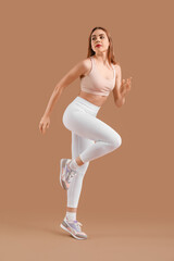 Beautiful young woman in sportswear training on brown background