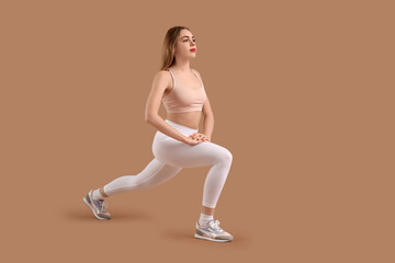 Beautiful young woman in sportswear training on brown background