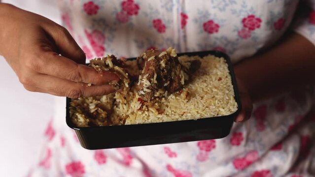 Women hand eating Mutton biryani. Packed box take away Chicken biryani Indian Malabar Kozhikode Hyderabadi biryani pulao Kerala India Pakistan basmati rice mixed rice dish meat curry Ramadan Eid