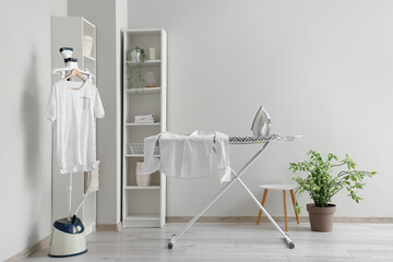 Interior of laundry room with garment steamer and ironing board - obrazy, fototapety, plakaty
