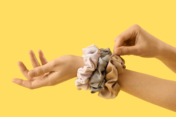 Female hands with stylish silk scrunchies on yellow background