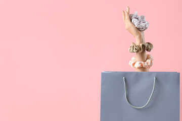 Female hand with silk scrunchies and shopping bag on pink background