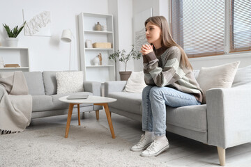 Young woman praying on sofa at home