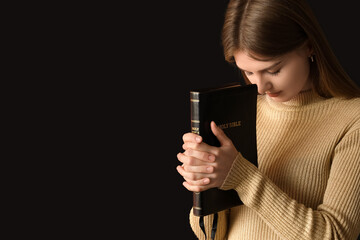 Young woman with Holy Bible praying on black background