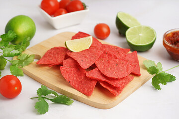 Wooden board with red nachos, lime and parsley on white background
