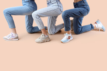 Female legs wearing different sneakers on beige background