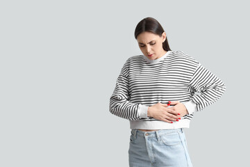 Young woman suffering from bellyache on light background