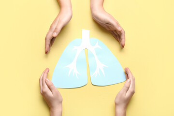 Hands of woman and child with paper lungs on yellow background
