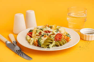 Delicious fusilli pasta with broccoli in plate, spices and glass of water on orange background, closeup