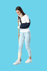 Injured young woman after accident with crutch walking on blue background