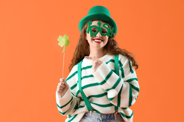 Young woman in Leprechaun's hat pointing at paper clover on orange background. St. Patrick's Day celebration
