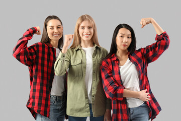 Fototapeta premium Beautiful young happy women showing muscles on grey background. Women history month