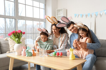 Happy family in bunny ears painting eggs at home on Easter Day