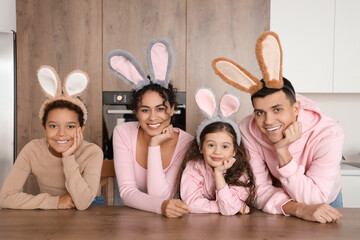 Happy family with bunny ears at table in kitchen on Easter Day