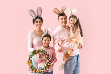 Happy family in bunny ears with Easter eggs and wreath on pink background
