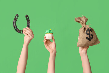 Female hands with tasty cupcake, horseshoe and money bag for St. Patrick's Day on green background