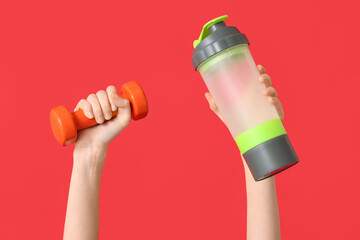 Female hands with bottle of water and dumbbell on red background, closeup