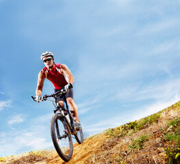Fototapeta premium Nature, fitness and man athlete with bicycle in park for marathon, race or competition training. Blue sky, sports and male cyclist riding bike for cardio workout or exercise in outdoor forest.