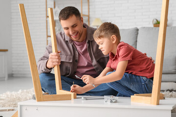 Happy father and his little son assembling table at home