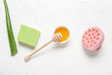 Hair scalp massager with shampoo bar, bowl of honey and aloe vera on white background