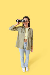 Young African-American woman looking through binoculars on yellow background