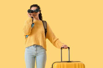 Female African-American traveler with map and suitcase looking through binoculars on yellow...