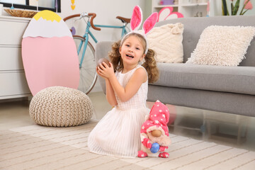 Cute little girl in bunny ears with chocolate Easter egg at home