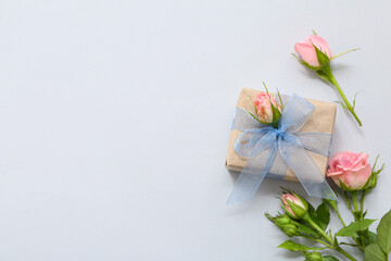 Elegant wrapped gift box with rose flowers decor on light background
