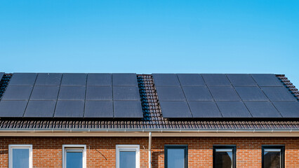 Fototapeta premium Newly built houses with black solar panels on the roof against a sunny sky Close up of new building with black solar panels. Solar panel, Sun Energy, Energy transition