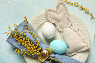 Beautiful table setting with Easter eggs and toy bunny on light blue background