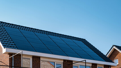 Newly built houses with black solar panels on the roof against a sunny sky Close up of new building with black solar panels in the Netherlands. Zonnepanelen, Zonne energie, Translation: Solar panel