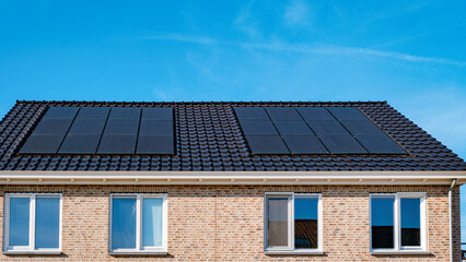 Fototapeta premium Newly built houses with black solar panels on the roof against a sunny sky, Close up of new building with black solar panels on a sunny day