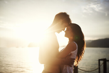 Sunset, couple and touch face at ocean for holiday, vacation or travel together in summer on lens flare. Happy man, woman and romance at sea for connection, care or love on adventure by water outdoor