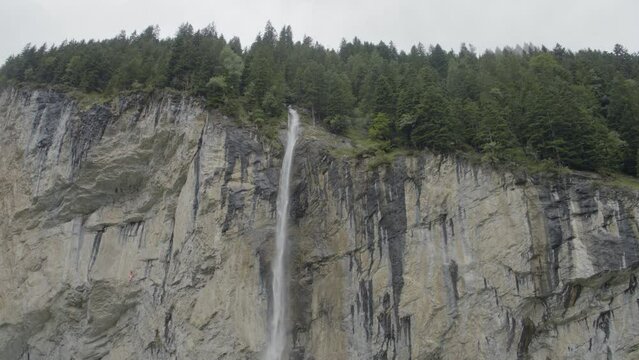 Majestic drone shot towards tall waterfall on massive Switzerland cliff