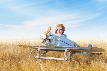 Little boy is playing the plane.
Happy and funy child imagines himself an aircraft pilot and plays in a aviator costume in an open-air field against a blue sky on a summer sunny day.  - 744370345