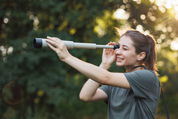 Young woman has a spyglass while standing in a forest at summer