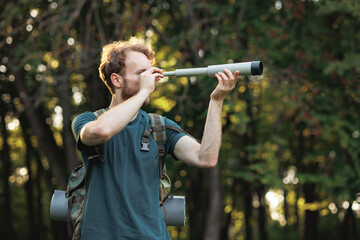 Young man has a spyglass while standing in a forest at summer