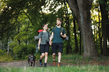 Photo of couple and a dog walking in forest at summer with backpacks