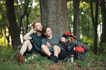 Fototapeta premium Photo of couple sitting in forest at summer with backpacks