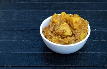 Potato Dahi Curd Curry or Aloo Gravy in a White Bowl Isolated on Black Wooden Background with Copy Space