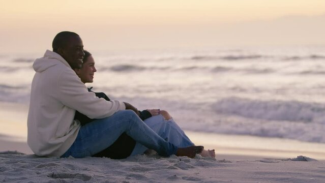 Shot of casually dressed loving young couple sitting on sand watching beautiful sunrise morning over beach and sea in South Africa - shot in slow motion