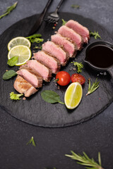 sliced grilled cooked piece of tuna fillet on black stone serving board